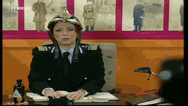 a woman wearing a fireman 's helmet sits at a desk in front of a wall with pictures of soldiers