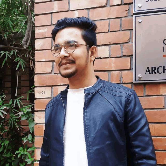 a man stands in front of a brick wall with a sign that says arch on it