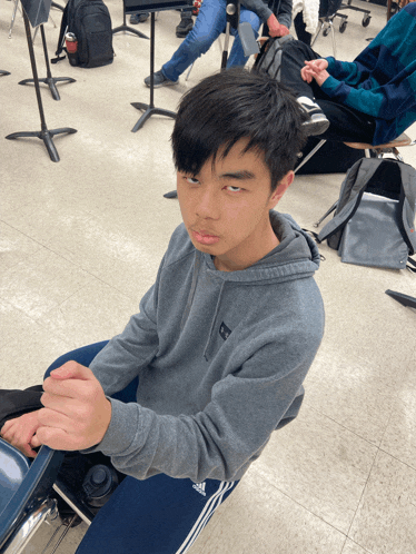 a young man wearing a grey adidas hoodie sits on the floor