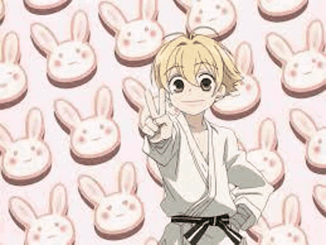 a boy in a karate uniform is giving a peace sign in front of a pattern of bunny cookies .