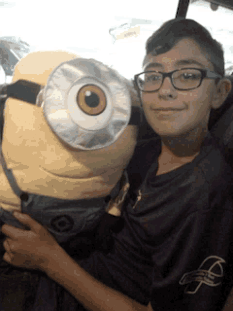 a boy in a purple shirt is holding a large stuffed minion