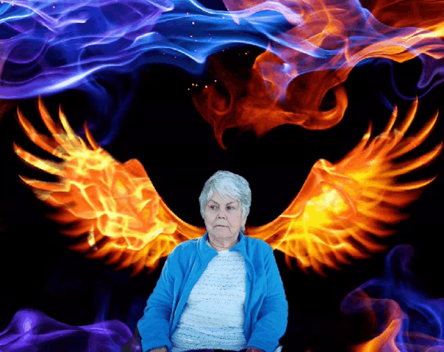 a woman in a blue jacket is sitting in front of a heart of flames