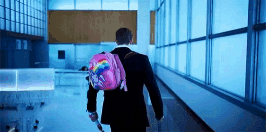 a man in a suit is walking down a hallway with a pink backpack and a suitcase .