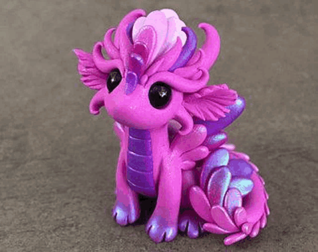 a purple and purple clay dragon figurine is sitting on a gray surface .