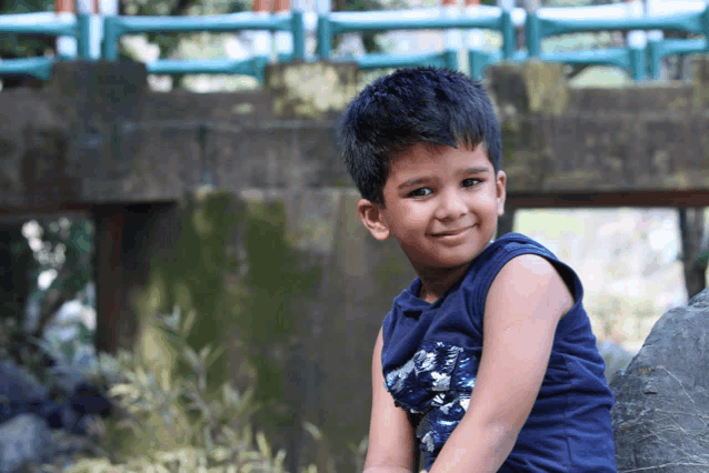 a young boy wearing a blue tank top is smiling for the camera