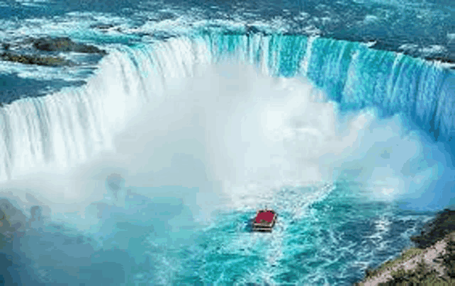 an aerial view of niagara falls with a red boat going underneath it .