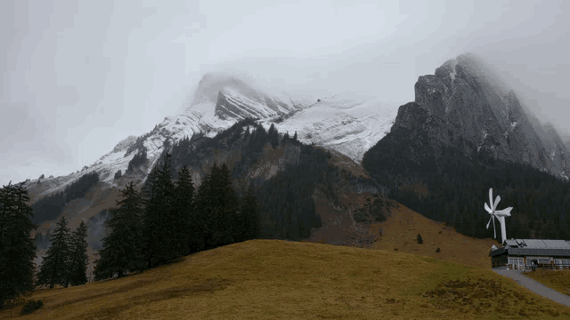 a windmill sits on a grassy hillside in front of a mountain