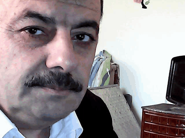 a man with a mustache looks at the camera in a room