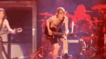 a man without a shirt is playing a guitar on stage in front of a drum set .