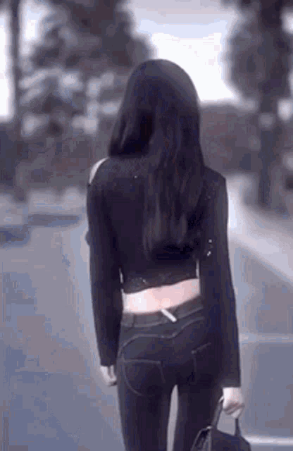 a woman in a black top and jeans is walking down the street .