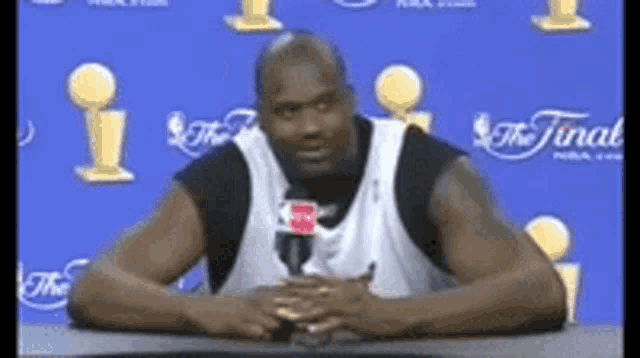 a man is sitting at a table with a microphone in front of a blue wall that says the finals