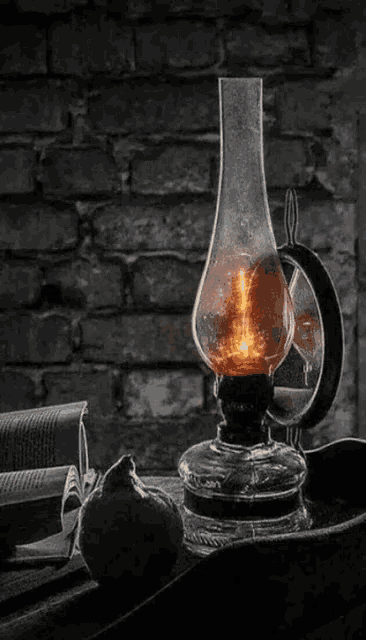 a black and white photo of an old oil lamp sitting on a table next to a brick wall .