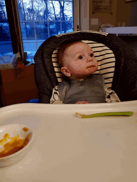 a baby is sitting in a high chair with a spoon in front of a box that says ' fragile ' on it