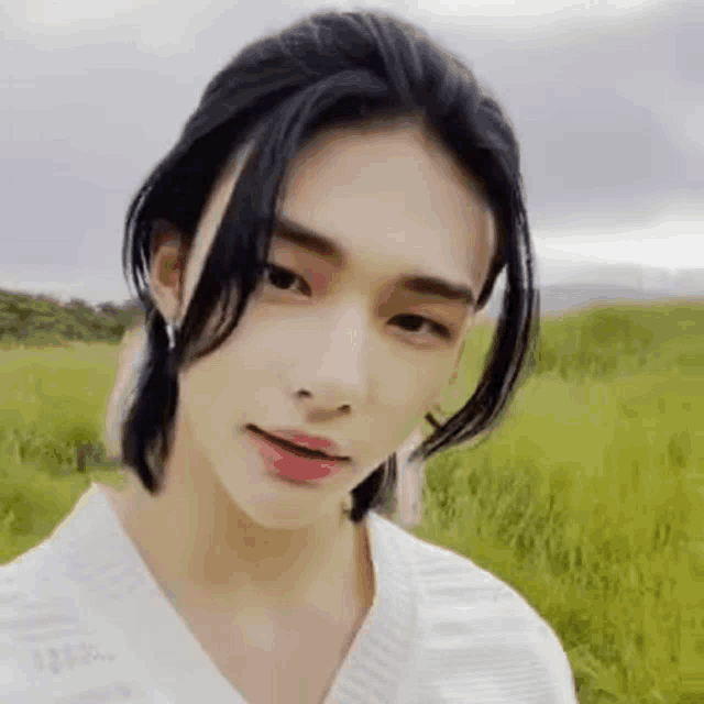 a young man with long black hair is standing in a field of tall grass .