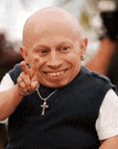 a bald man wearing a necklace with a cross on it is smiling and giving a peace sign .