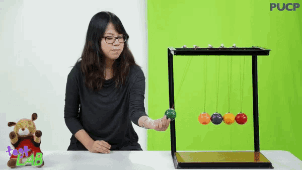 a woman is playing with a newton 's cradle in front of a green wall with pucp written on it