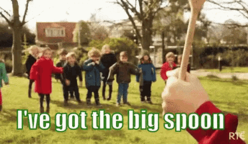 a group of children are playing in a park with a person holding a big spoon in front of them .