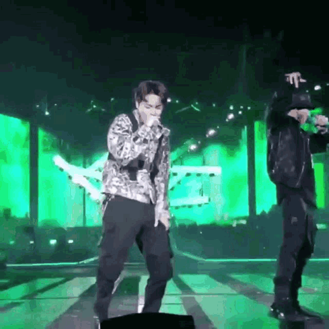 a man is singing into a microphone on a stage while another man is dancing .