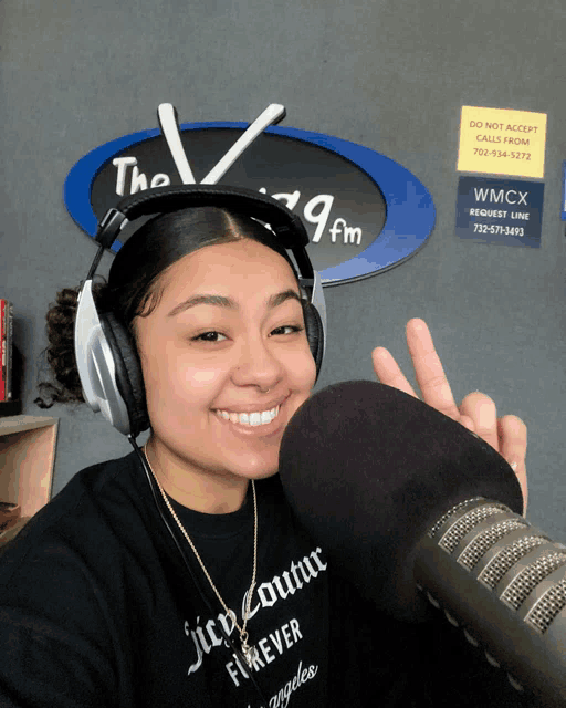 a woman wearing headphones and a shirt that says juicy couture forever stands in front of a microphone