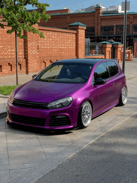 a purple car is parked on a sidewalk in front of a brick wall