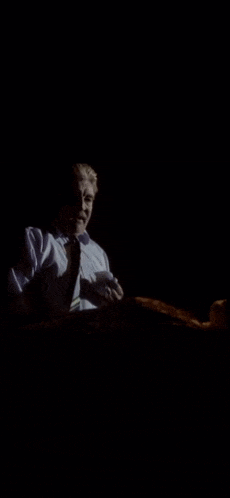 a man in a white shirt and tie is sitting in the dark and smiling