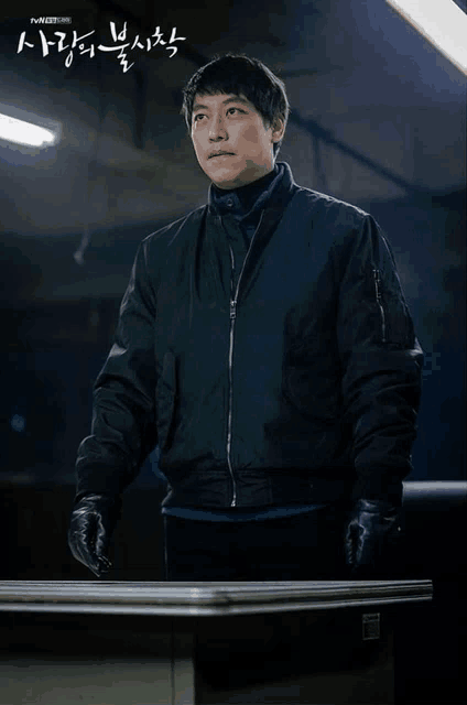 a man in a black jacket and black gloves is standing in front of a table