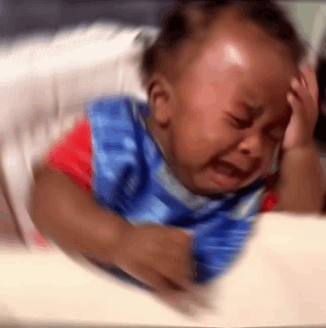 a baby is crying in a high chair while holding his head .