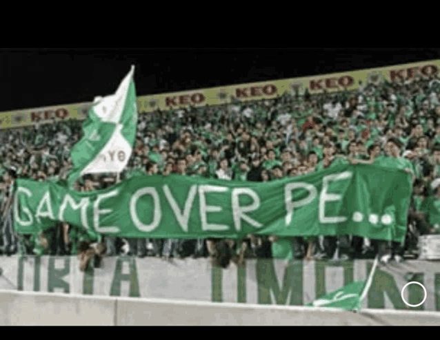 a stadium full of people holding a green banner that says game over pe