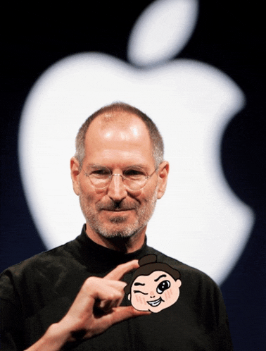 a man wearing glasses holds up a small cartoon face in front of an apple logo