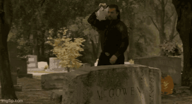 a man is standing in front of a gravestone with the name mcgowen written on it .