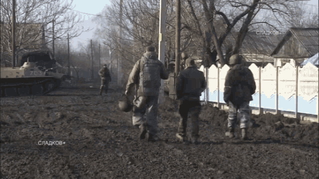 a group of soldiers are walking in a field with a tank in the background that has the number 766 on it