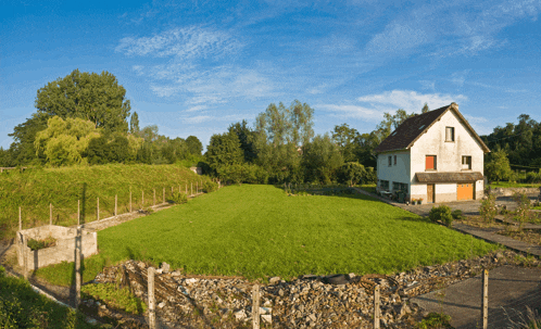 a white house with a red door sits in the middle of a green field