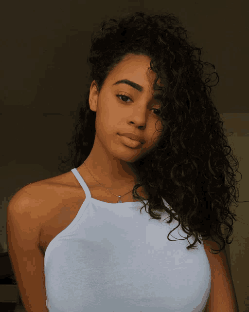 a woman with curly hair wears a white tank top