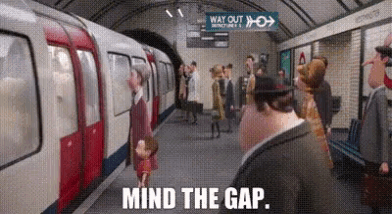 a group of people are waiting for a train at a subway station and the caption reads mind the gap .