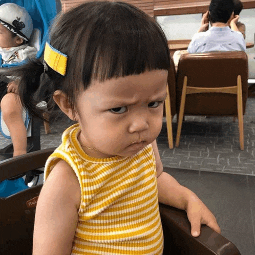 a little girl wearing a yellow and white striped shirt is sitting in a high chair