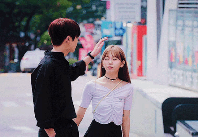 a man touches a woman 's forehead while they are walking down the street