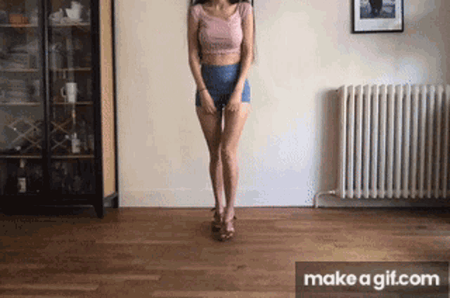 a woman in a pink top and blue shorts is standing in front of a radiator in a living room ..