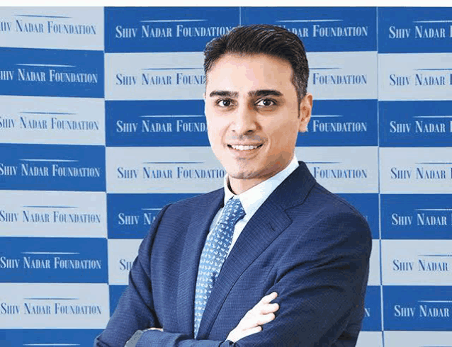 a man in a suit and tie stands in front of a wall that says shiv nadar foundation