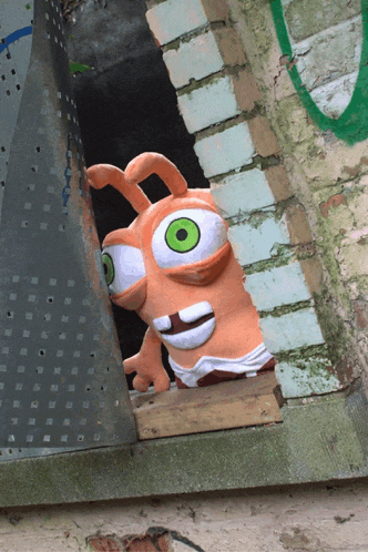 a stuffed animal with green eyes looks out of a hole in a wall