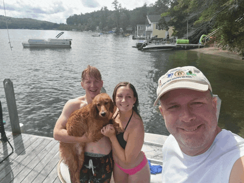 a man wearing a hat with the letter r on it poses with two people and a dog on a dock