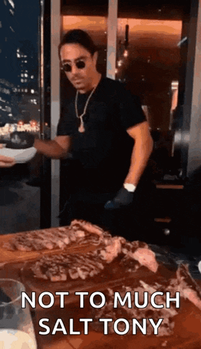 a man is standing in front of a table with a plate of food and a cutting board with meat on it .