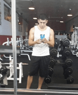 a man taking a picture of himself in a gym with a row of dumbbells behind him