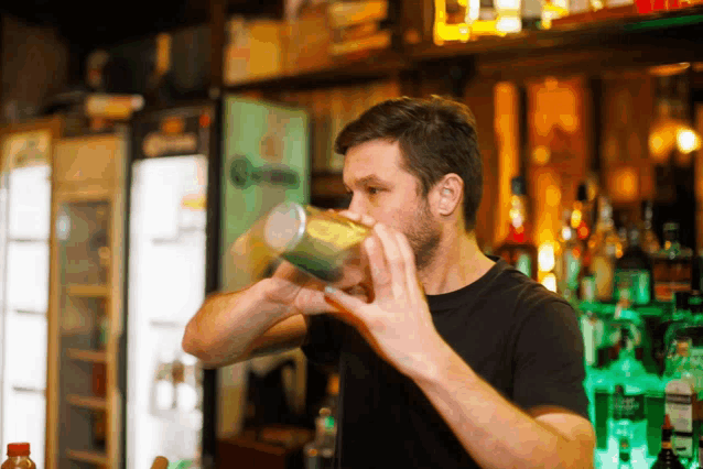 a man in a black shirt is shaking a drink in front of a corona beer fridge