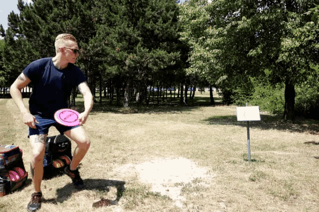 a man is throwing a frisbee in a field with trees in the background and a sign that says " a "