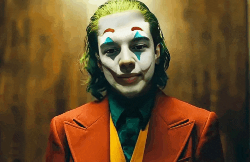 a young man dressed as the joker in a red suit and tie is smiling .