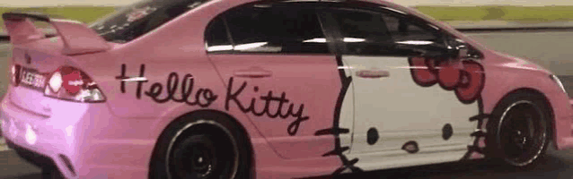 a pink hello kitty car is driving down the street .