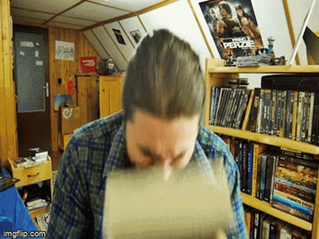 a man in a plaid shirt is drinking from a cup in front of a bookshelf with a star wars poster on it