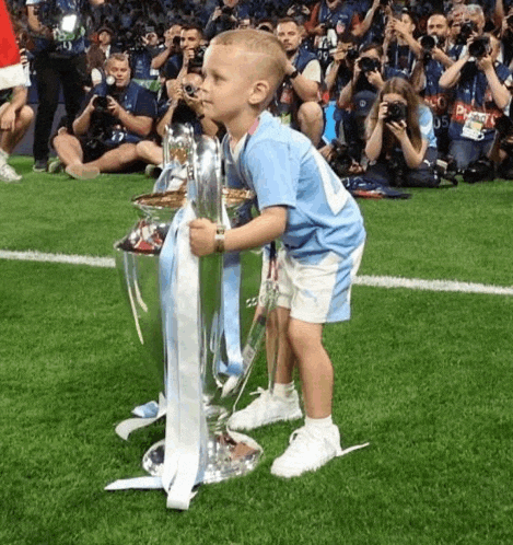 a young boy holds up a trophy on a soccer field