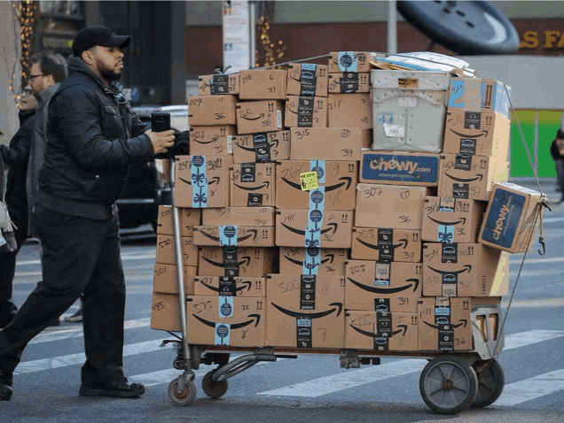 a man pushes a cart full of amazon boxes on the street