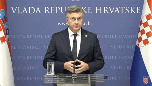 a man in a suit and tie stands at a podium in front of a wall that says vlada republike